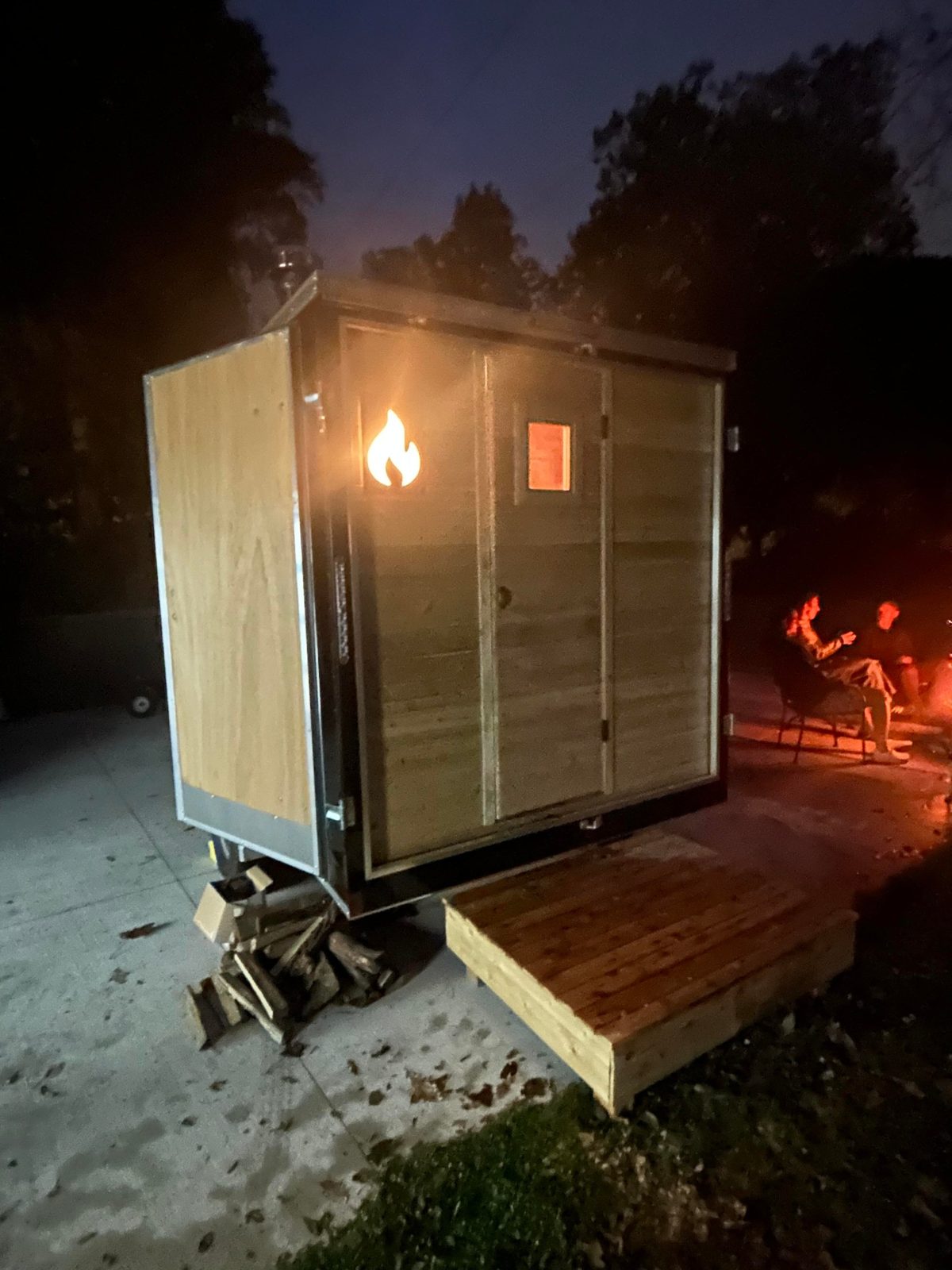 Dusk shot of the Thermic sauna with the flame logo glowing from within, a fire burning nearby.
